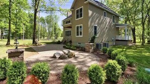 A two-story house with a covered porch, surrounded by a landscaped garden with shrubs and a stone pathway. - Riverfront on the Hudson with nature to explore (Mechanicville)
