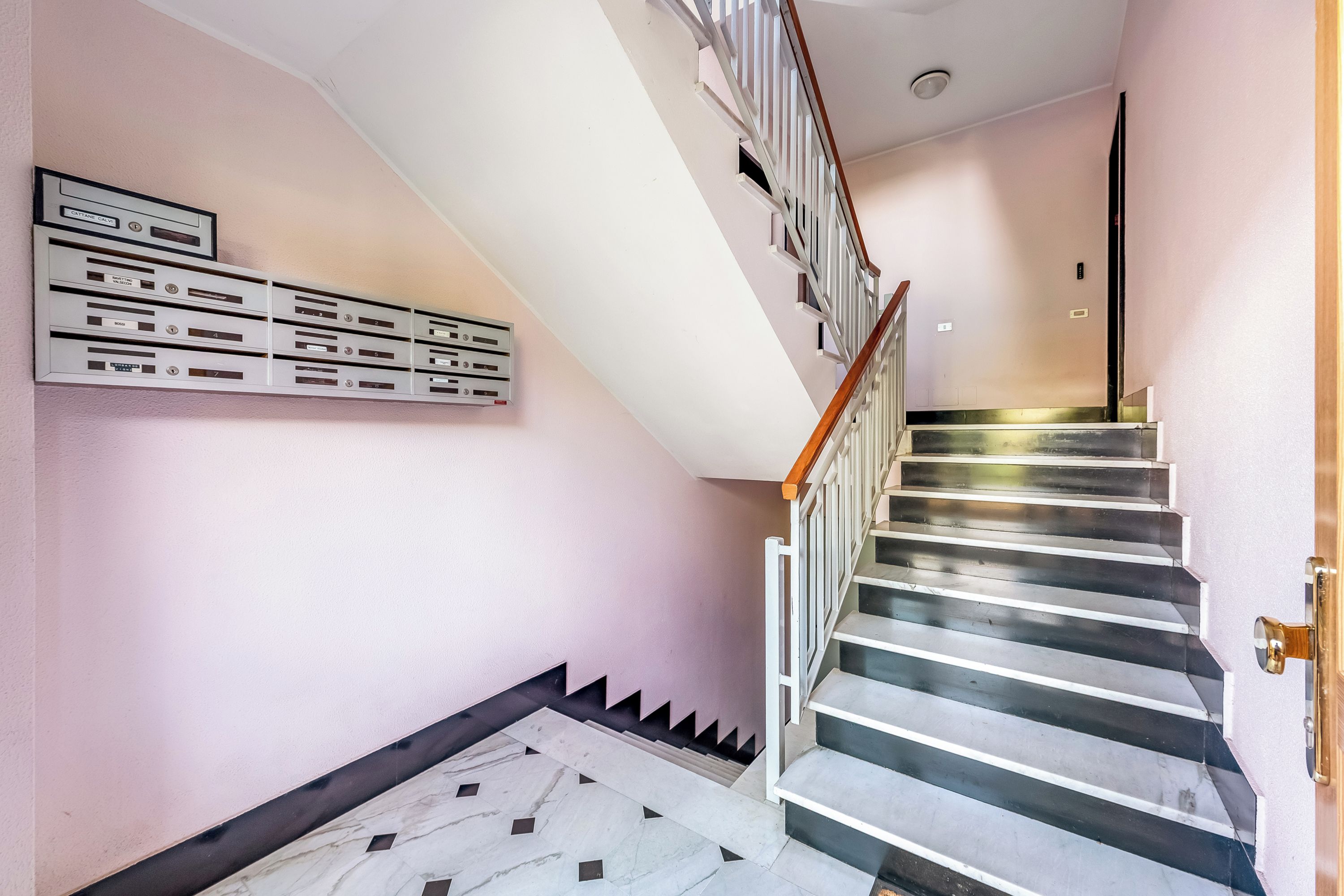 A staircase with a handrail, a marble floor, and a wall-mounted mailbox.