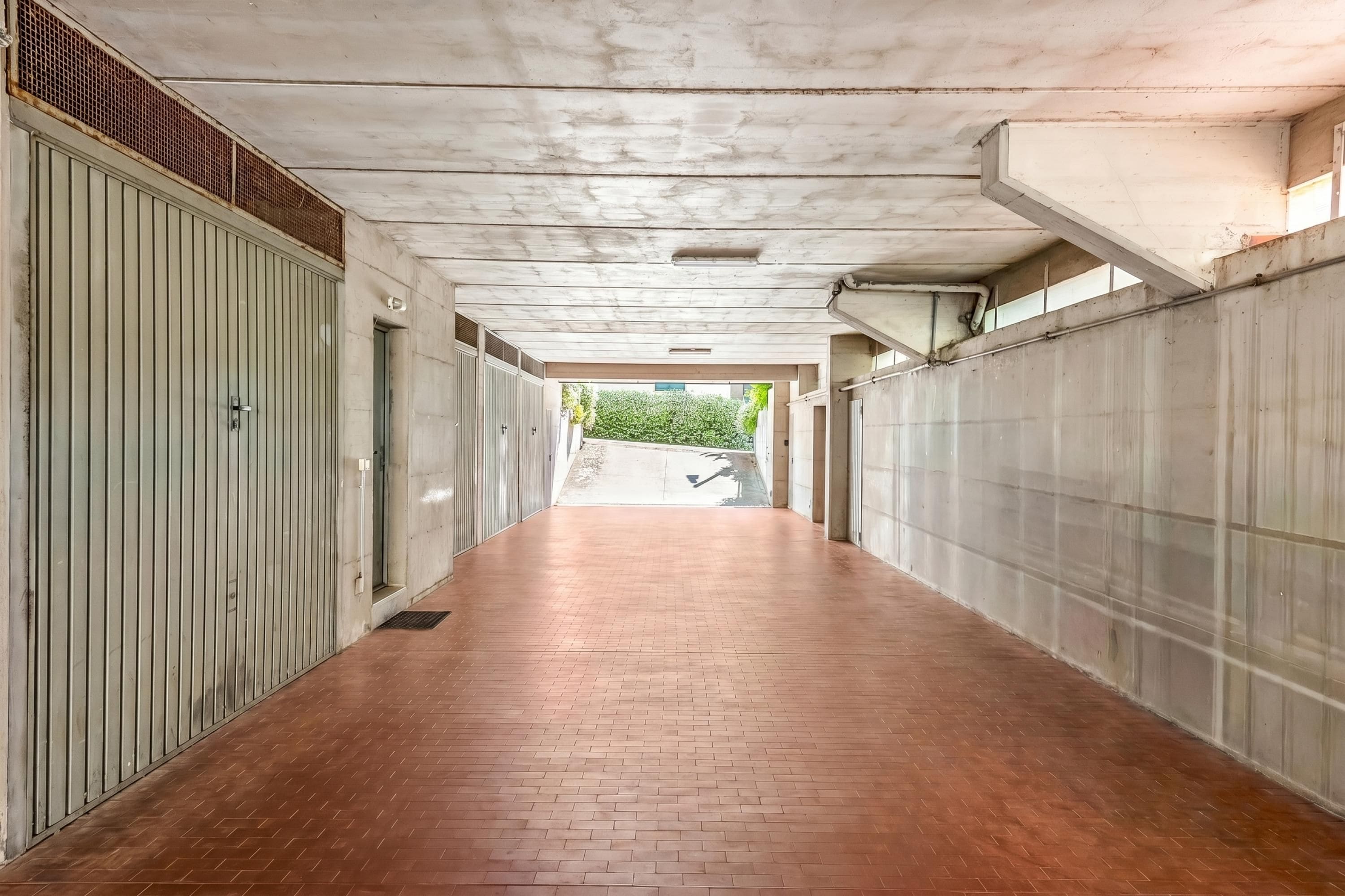 Un couloir doté d’un sol carrelé, de portes métalliques et d’un plafond en béton.