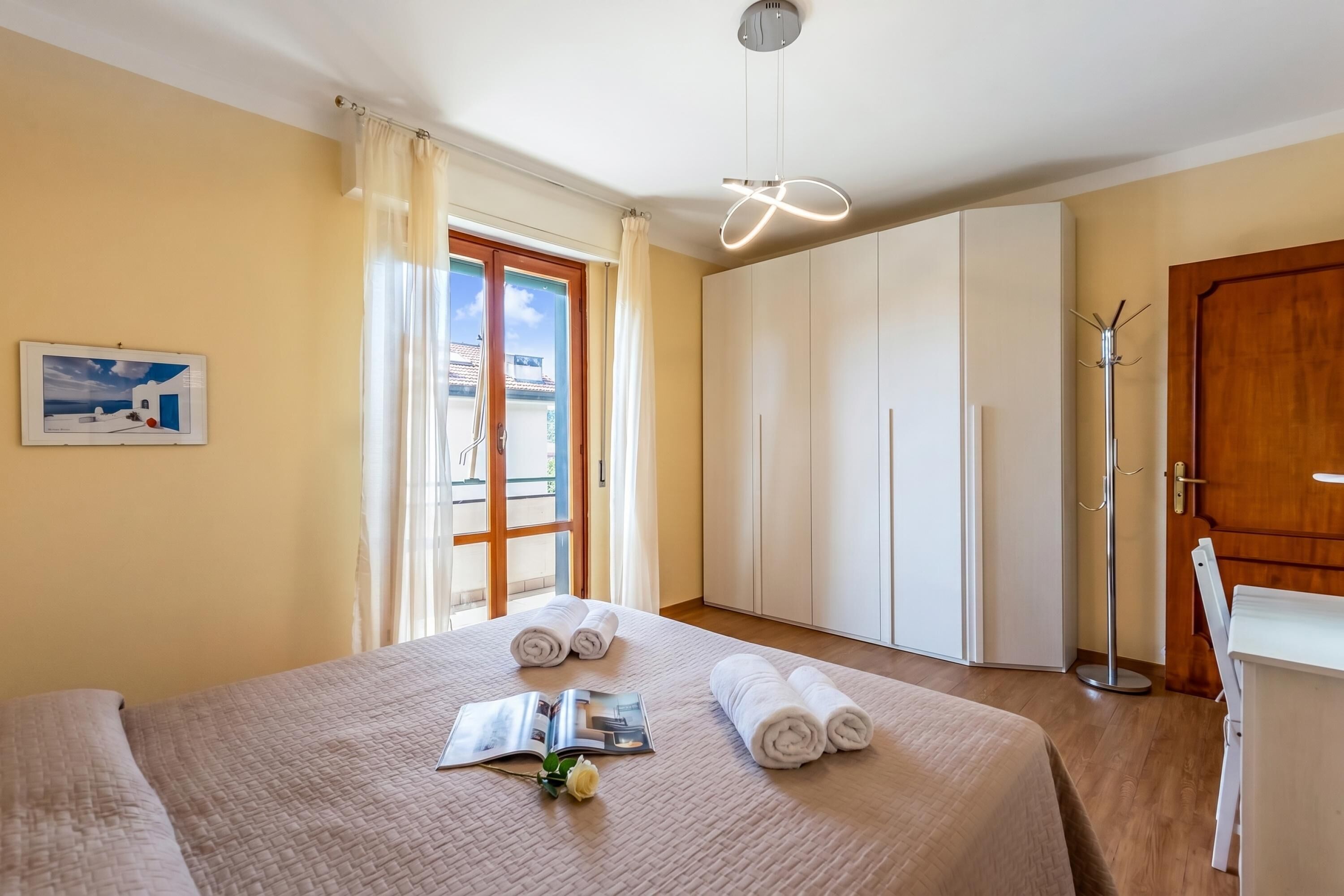 Habitación de hotel con cama, mesita de noche, lámpara, armario y vistas al exterior.