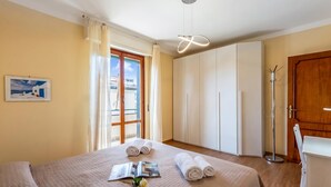 A hotel room with a bed, a bedside table, a lamp, a wardrobe, and a view of the outside. - Il Forte - Apartment With Balcony (Sestri Levante)