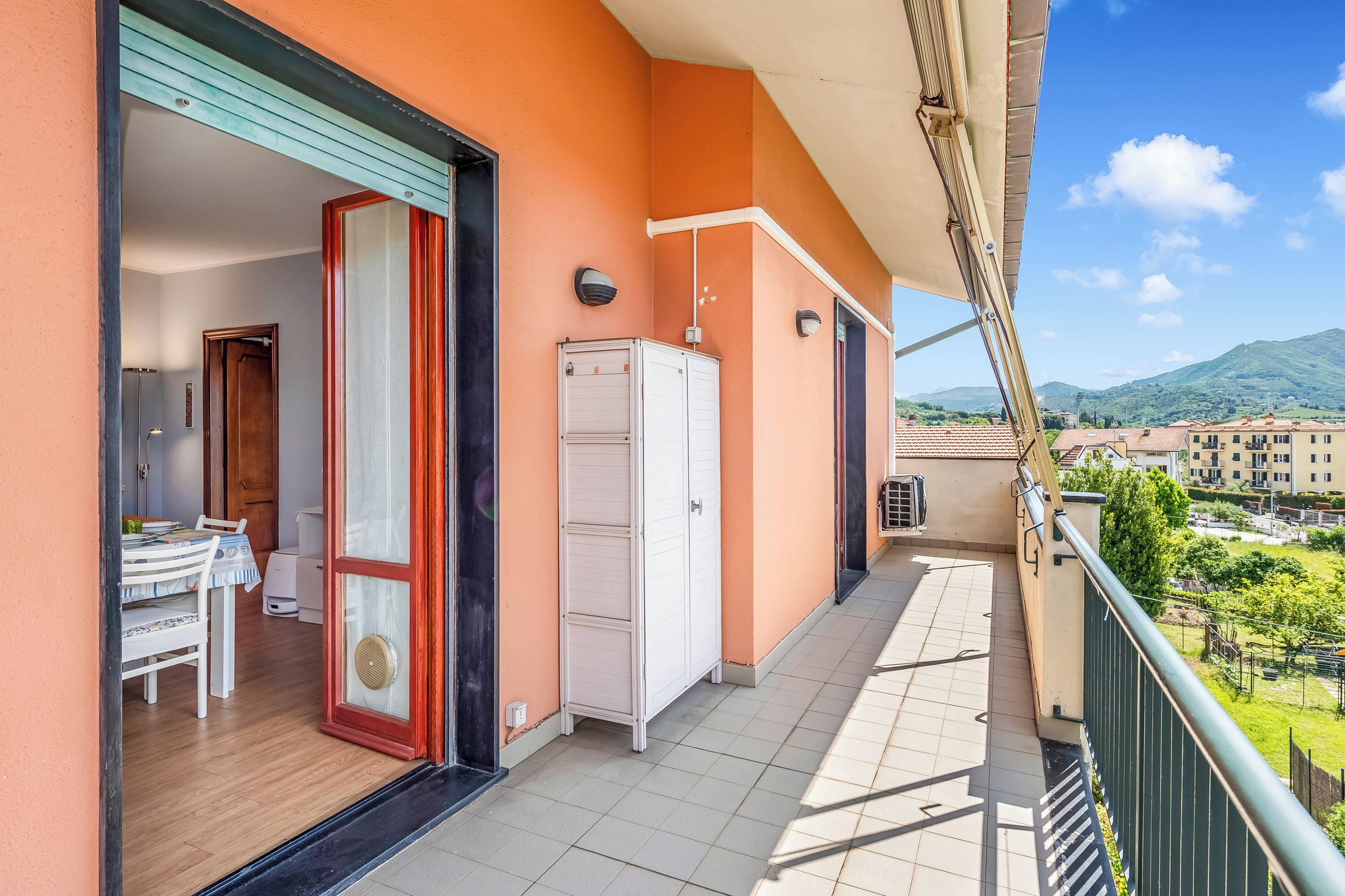 Un balcon donnant sur un paysage montagneux, un meuble blanc et un coin repas avec une table et des chaises.