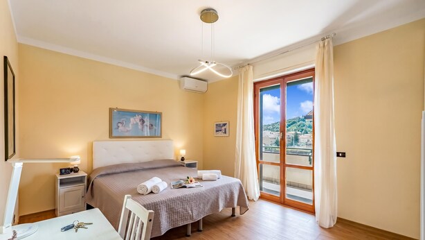 A hotel room with a bed, bedside tables, a desk, a chair, a window with curtains, and a view of the outside. - Il Forte - Apartment With Balcony (Sestri Levante)