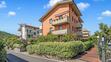 Um edifício residencial com várias andares, varandas, entrada pavimentada e um hedge verde.
