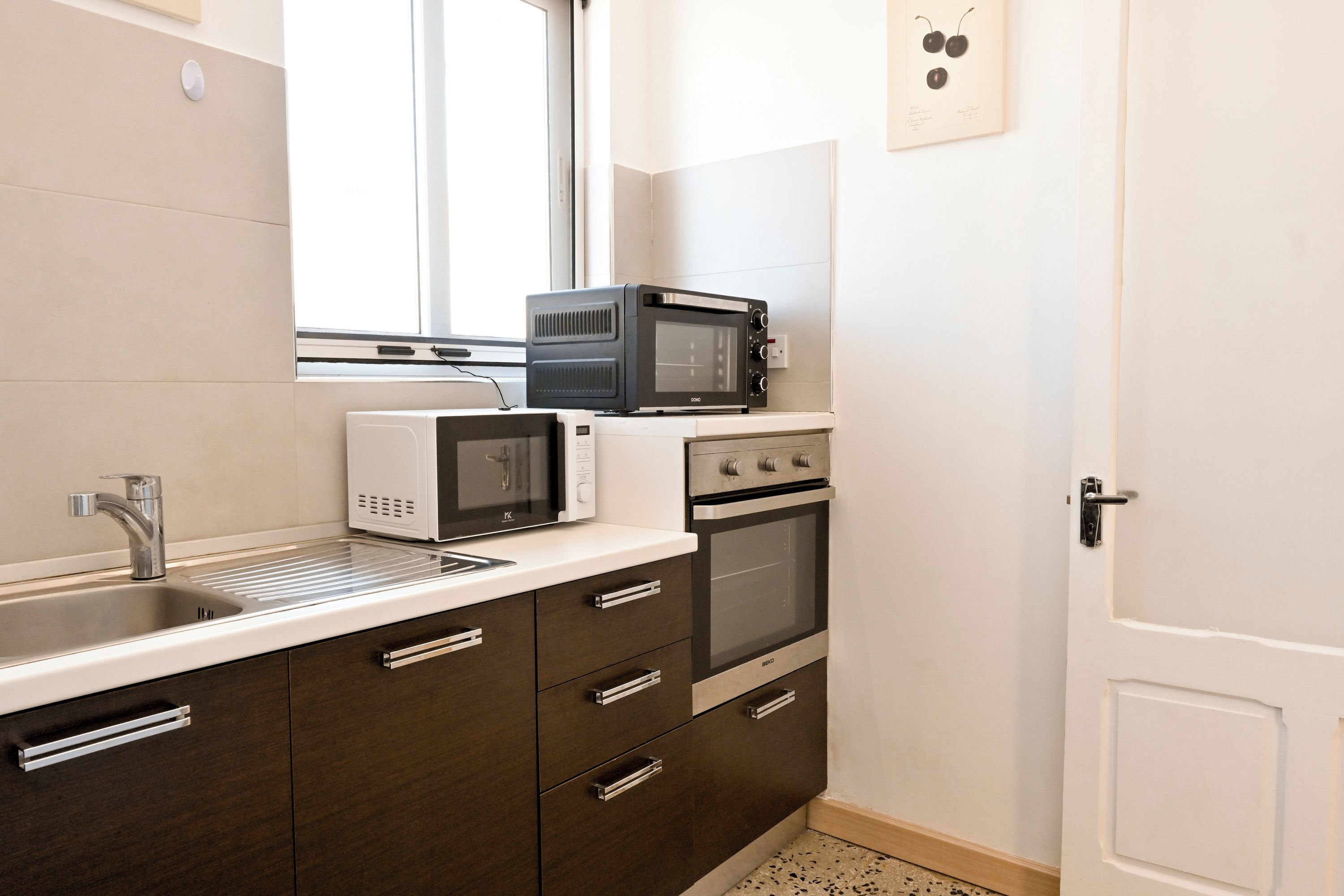 Cocina compacta con lavamanos, microondas blanco y horno de acero inoxidable.