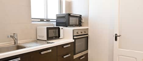 Cocina compacta con lavamanos, microondas blanco y horno de acero inoxidable.