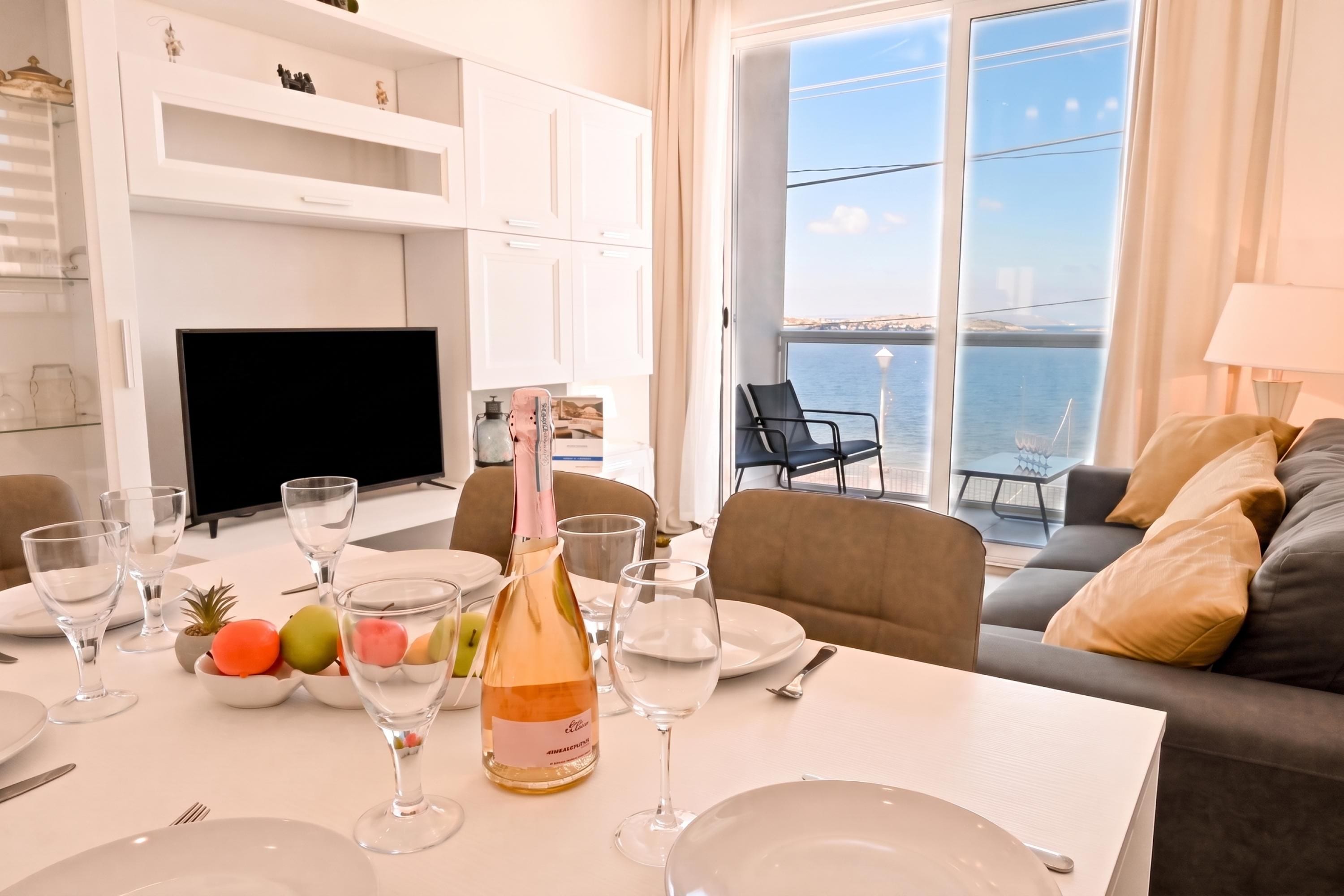 Un comedor con una mesa dispuesta para dos personas, una botella de champán y vistas al mar a través de amplios ventanales.