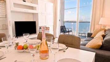 Un comedor con una mesa dispuesta para dos personas, una botella de champán y vistas al mar a través de amplios ventanales.