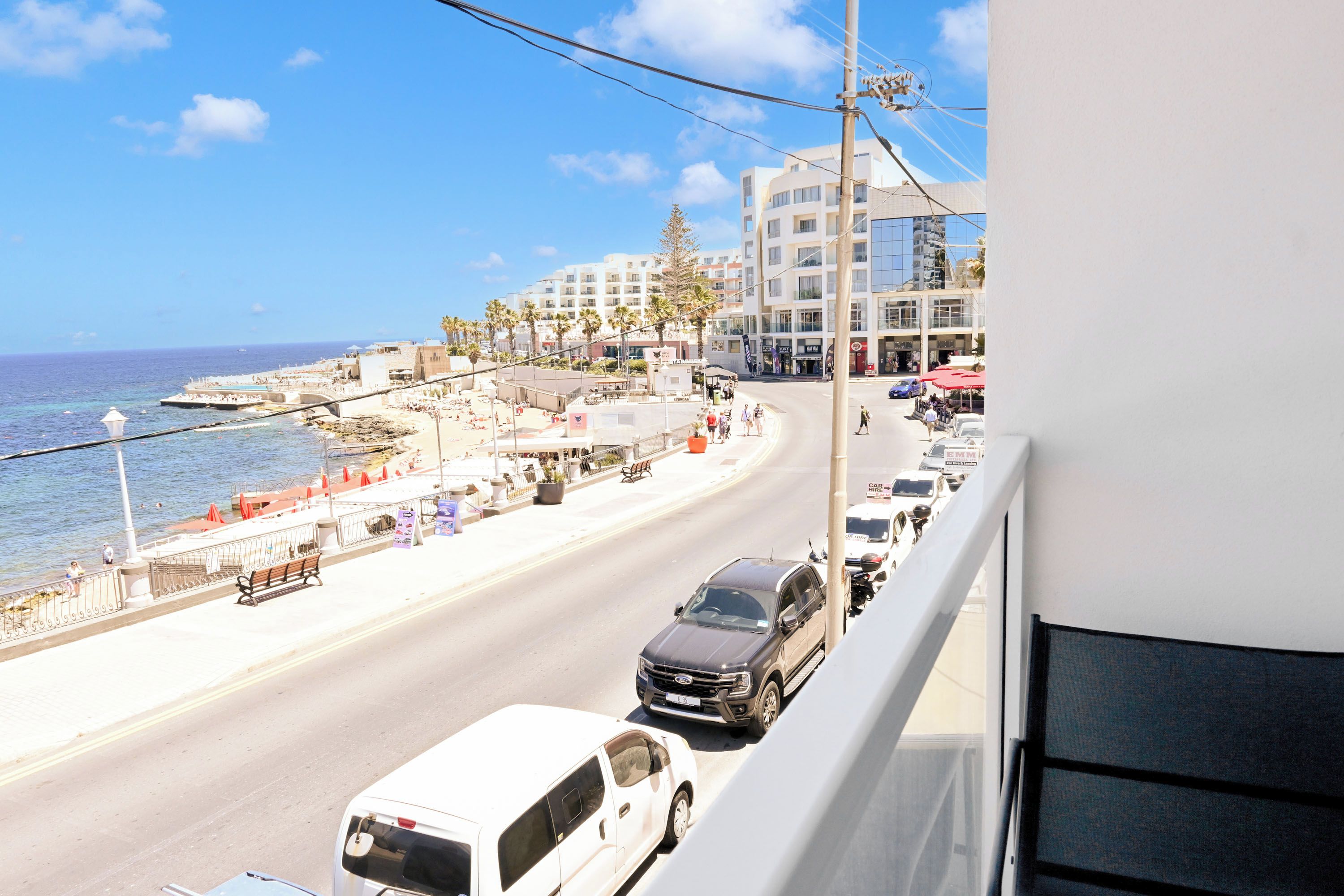 Eine Küstenstraße mit Fahrzeugen, einem Strand und Gebäuden im Hintergrund.