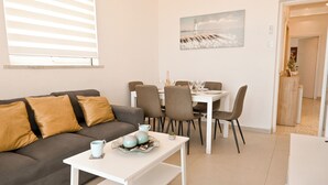 A modern living room with a sofa, a dining table with chairs, and a painting on the wall. - Exceptional Sea View Apart St Paul's Bay (St. Paul's Bay)