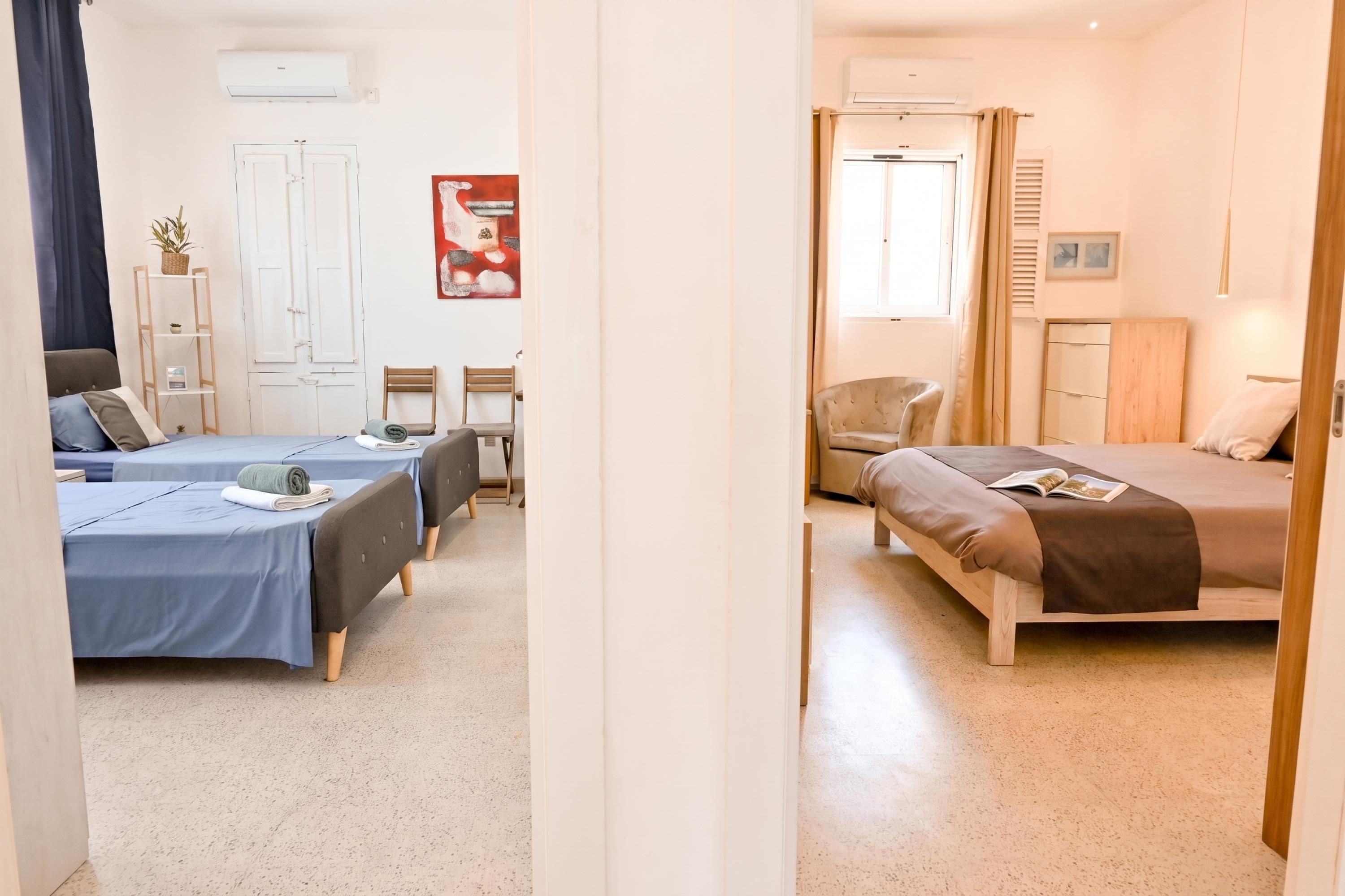 A hotel room with two beds, a wardrobe, a chair, a small table, and a potted plant.