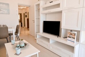 A modern living room with a flat-screen TV, white cabinetry, a dining area with a table and chairs, and a hallway leading to another room. - Exceptional Sea View Apart St Paul's Bay (St. Paul's Bay)