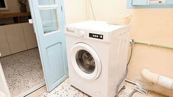 Una lavadora compacta y blanca de carga frontal en un pequeño cuarto de lavado con piso de baldosas y una puerta azul.