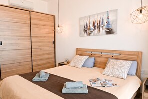 A bedroom with a wooden bed frame, two pillows, a blanket, and a magazine on the bed. There is a wooden wardrobe and a painting on the wall. - Exceptional Sea View Apart St Paul's Bay (St. Paul's Bay)