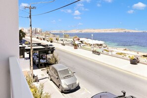A coastal street with a parked car, outdoor seating at a restaurant, and a view of the sea. - Exceptional Sea View Apart St Paul's Bay (St. Paul's Bay)
