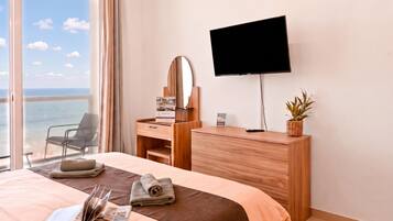 Habitación de hotel con cama, escritorio con televisor de pantalla plana, una silla, ventana con vista al mar y planta en maceta.