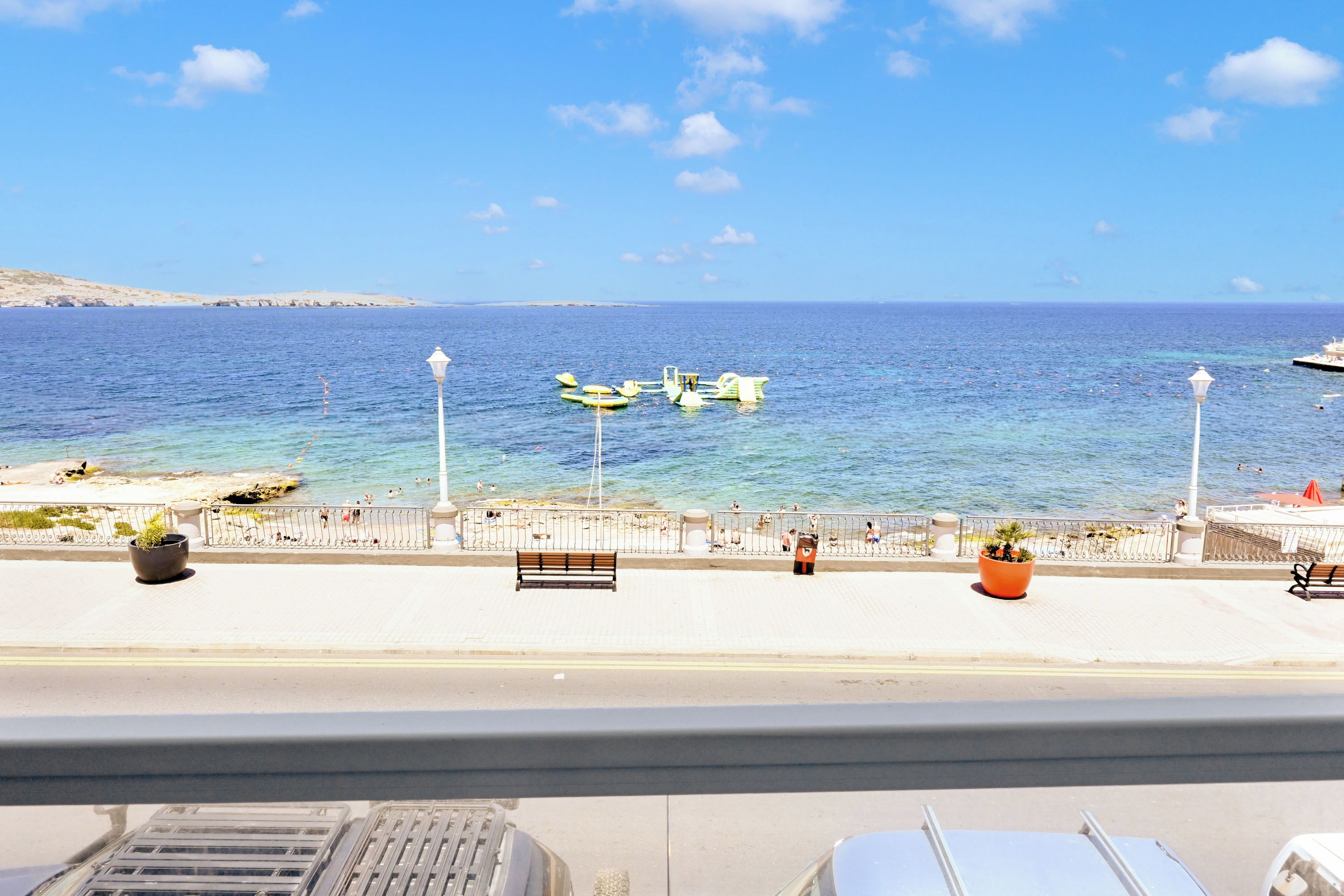 Un paseo marítimo con vistas despejadas al mar, algunas embarcaciones y un banco a lo largo del camino.