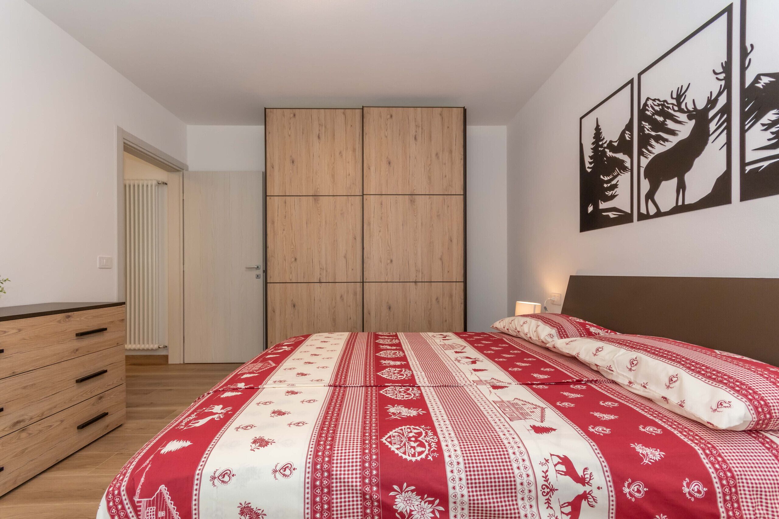 A bedroom with a bed, a dresser, a wardrobe, and a wall with framed pictures.