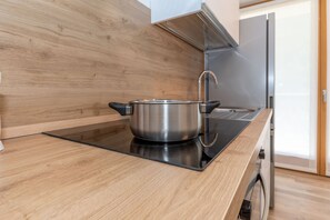 Une cuisine moderne avec une casserole en acier inoxydable sur une plaque de cuisson à induction, des meubles en bois et une hotte en acier inoxydable.