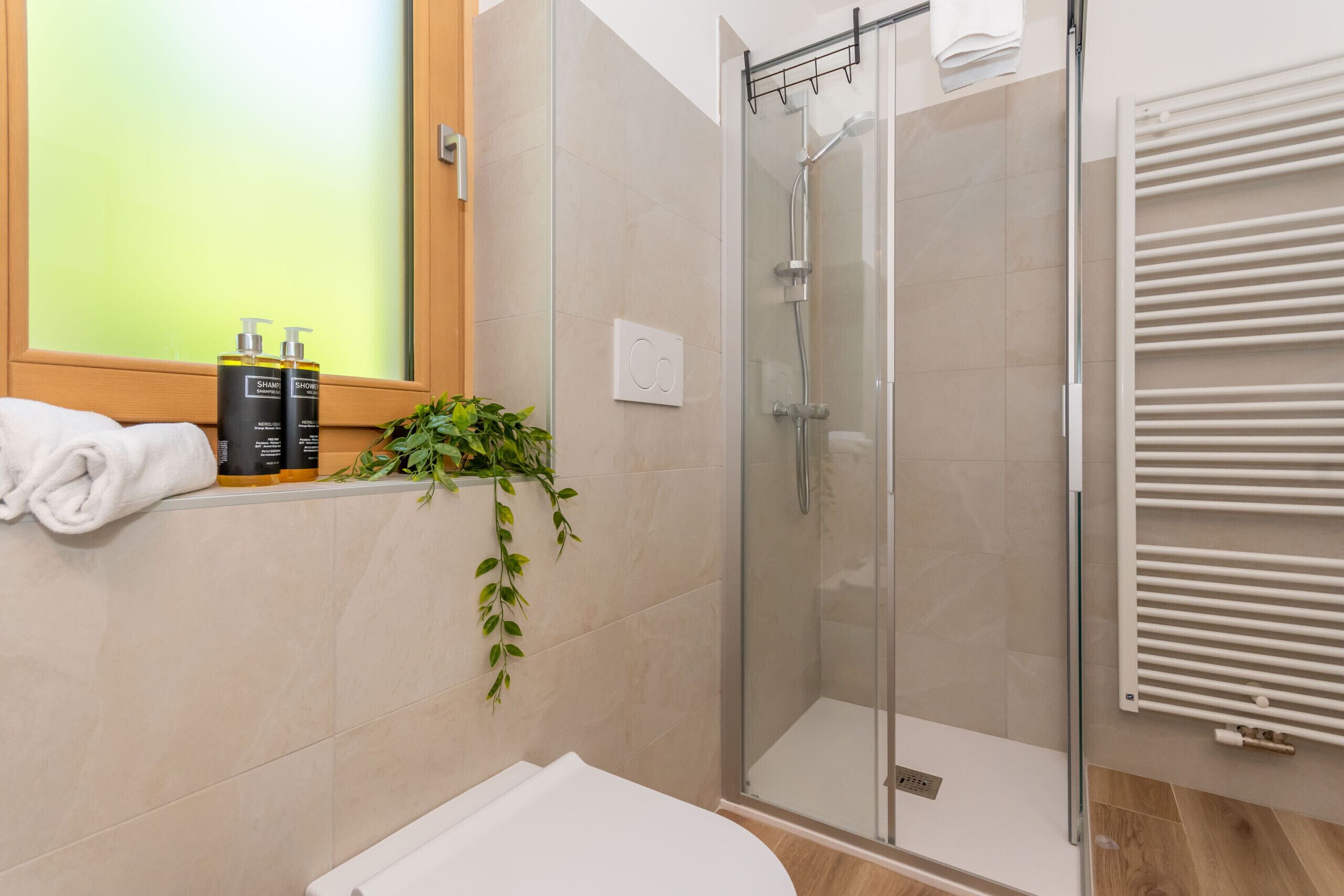A modern bathroom with a glass shower enclosure, a white toilet, and a window with a view.