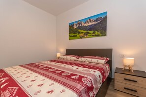 Een slaapkamer met een bed, twee bedlampjes, een nachtkastje, een lade en een wandeling berglandschap.
