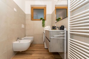 Een moderne badkamer met een toilet, wasmachine en een bidet, met een houten raam en een handdoekhouder.