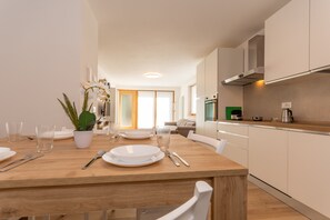 Una cocina moderna con armarios blancos, una mesa de comedor de madera dispuesta con platos, vasos y cubiertos, y una planta en maceta.