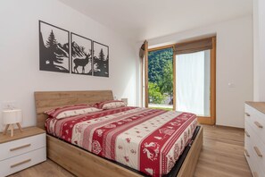Een slaapkamer met een houten bed, een nachtkastje, een kast en een raam met uitzicht op groen.