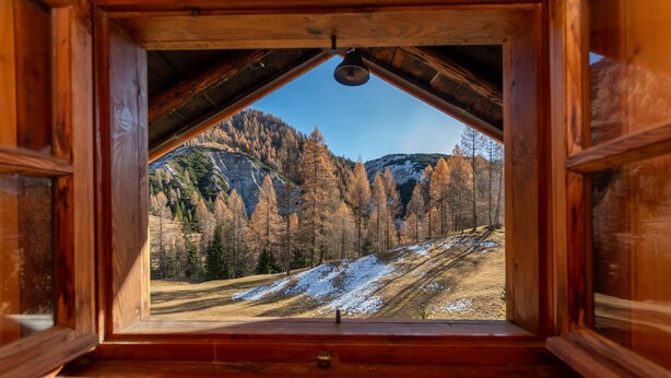 A wooden cabin with a triangular roof and a view of a mountainous landscape.