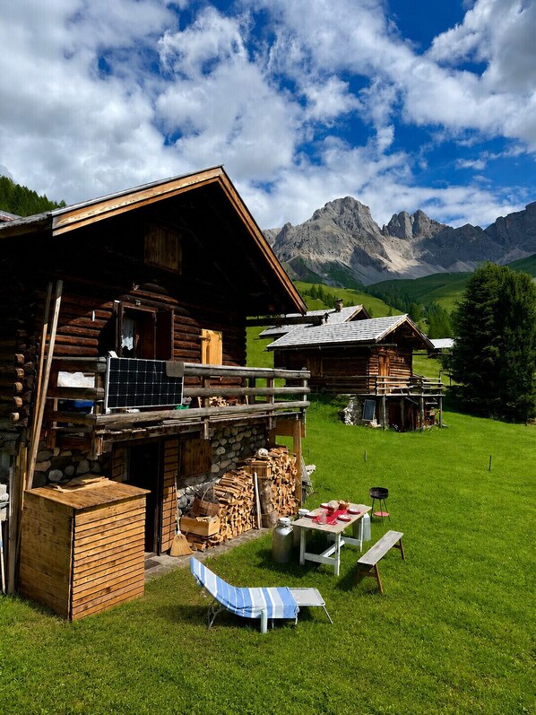 A wooden log cabin with a balcony, a stack of firewood, and a table with chairs outside.