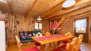 A wooden interior with a dining table, chairs, a sofa, and a staircase.