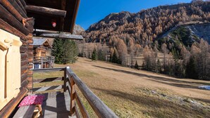 A wooden cabin with a deck, a view of a forested mountain, and a clear sky.