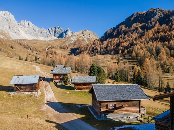 Ein Bergdorf mit Holzhäusern, einer unbefestigten Straße und einer Bergkulisse im Hintergrund.