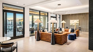 A modern hotel lobby with a seating area, large windows, and a view of the city. - C.R.E.A.M & Cocoa | Resort Pool, Laundry, Parking (Dallas)