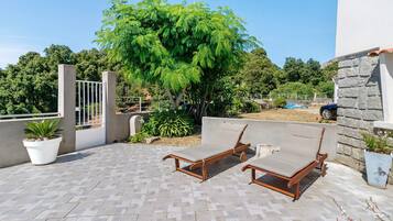 A patio with two wooden lounge chairs, a potted plant, and a stone wall.