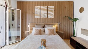 Een moderne slaapkamer met een wand van houten latten, een bed met veel kussens, een nachtkastje, een grote plant en een glazen deur naar een balkon.