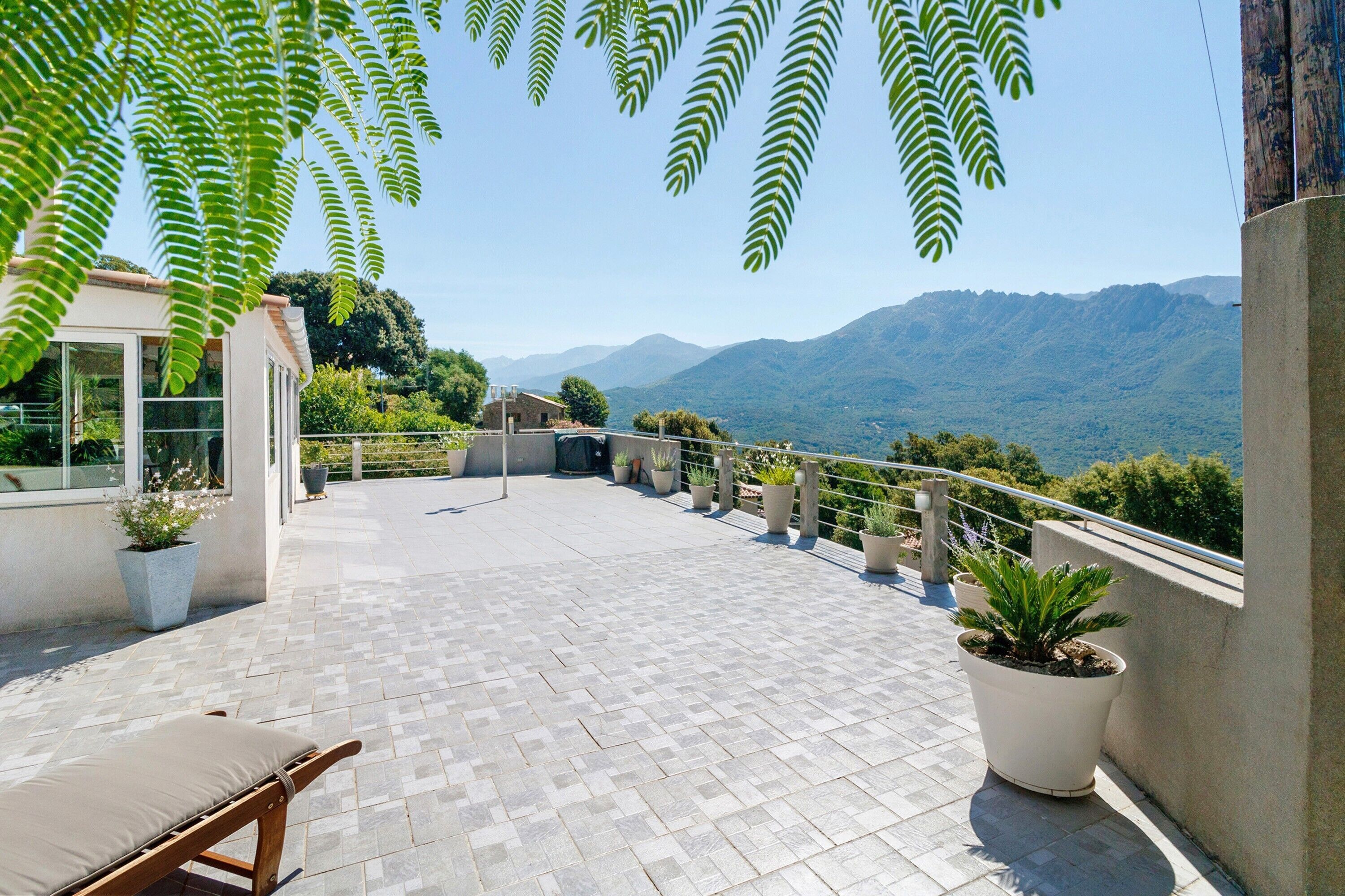 Une terrasse agrémentée de plantes en pot, d’un banc et offrant une vue sur les montagnes.