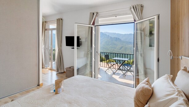 Een slaapkamer met een groot bed, een televisie en een balkon met uitzicht op bergen.