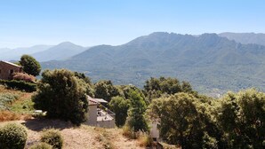 A rural landscape with a house surrounded by trees and mountains in the background.