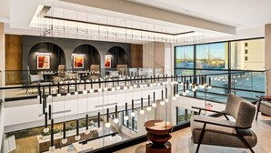 Eine moderne Hotelhalle mit Glasgeländer, Sitzgelegenheiten und Blick auf die Stadt.