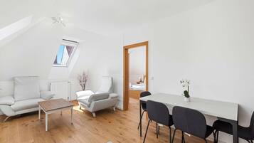 Un appartement moderne de style « loft » avec un plafond en pente, un coin repas comprenant une table et des chaises blanches, un canapé blanc et une table basse en bois.