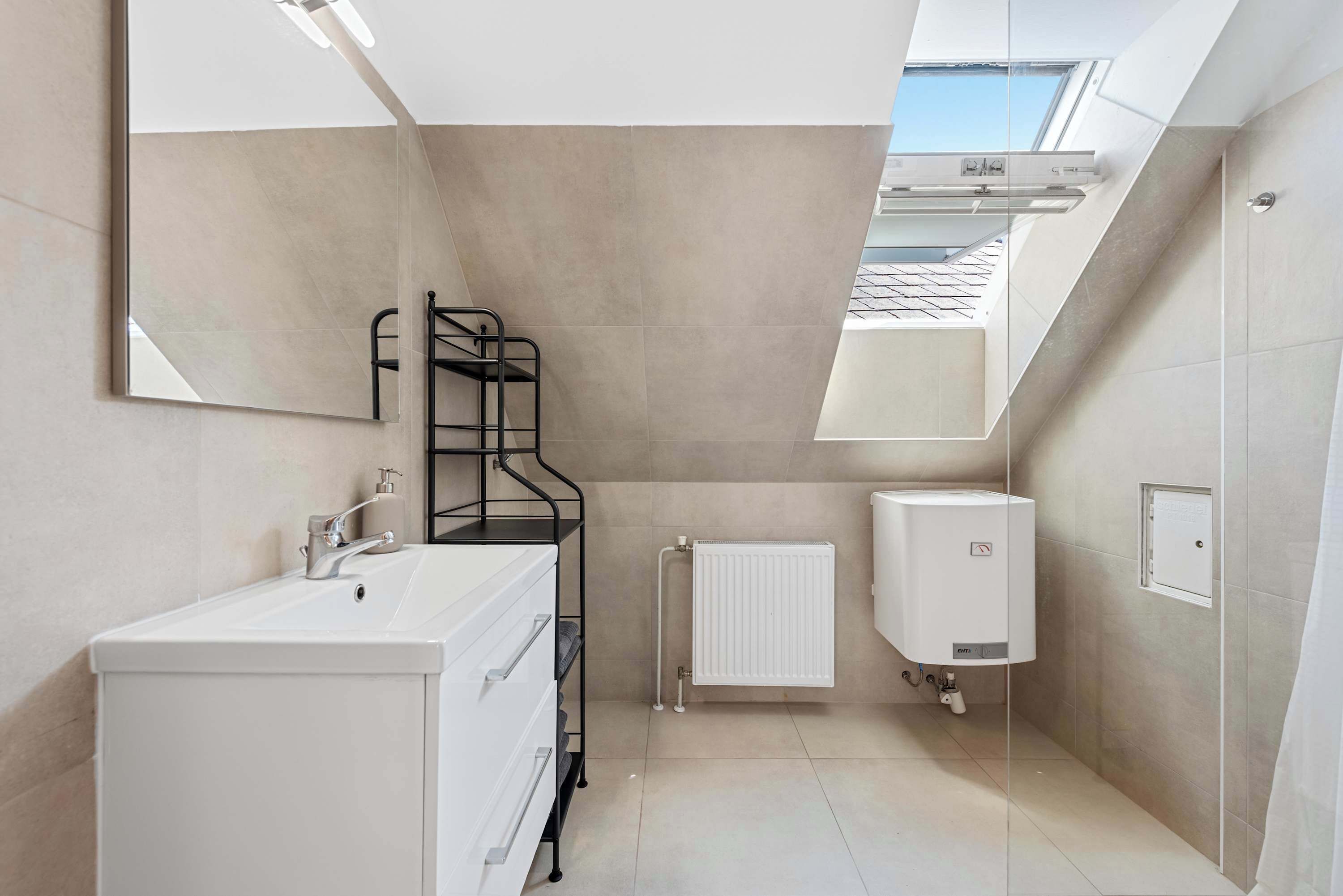 Un baño moderno con tragaluz, sanitarios blancos y radiador.