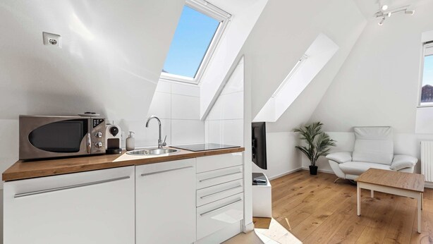 Una cocina moderna con tragaluz, armarios blancos, un microondas y un lavabo.