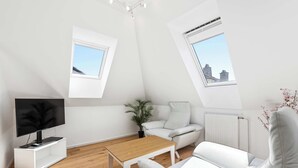 Una sala de estar moderna con televisor, sofá blanco, mesa de centro de madera y una planta en maceta.
