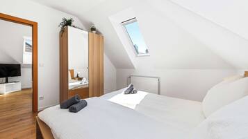 A bedroom with a sloped ceiling, a skylight, a bed with pillows, a TV, and a wooden wardrobe.