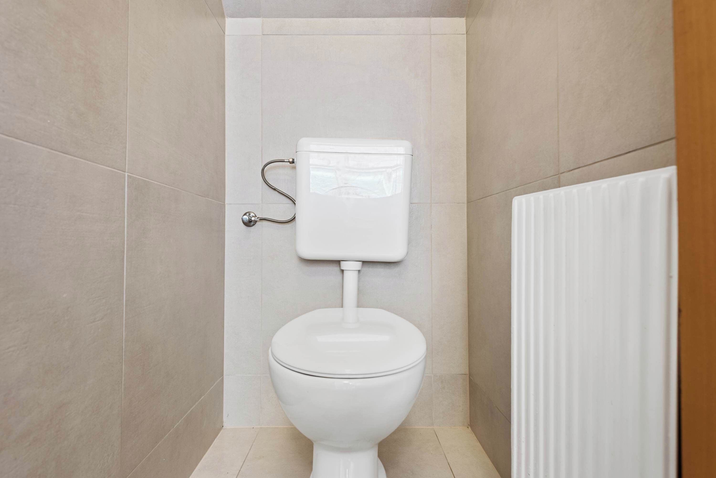 Sanitário branco em um banheiro com azulejos bege.
