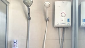 A bathroom with a shower, a handheld showerhead, a wall-mounted showerhead, and a water heater. - Butnamtong Hotel (Lampang)