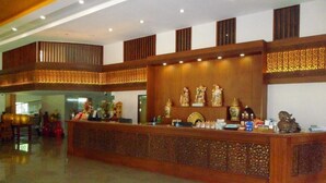 A reception area with a wooden counter, decorative statues, and a patterned wall. - Butnamtong Hotel (Lampang)