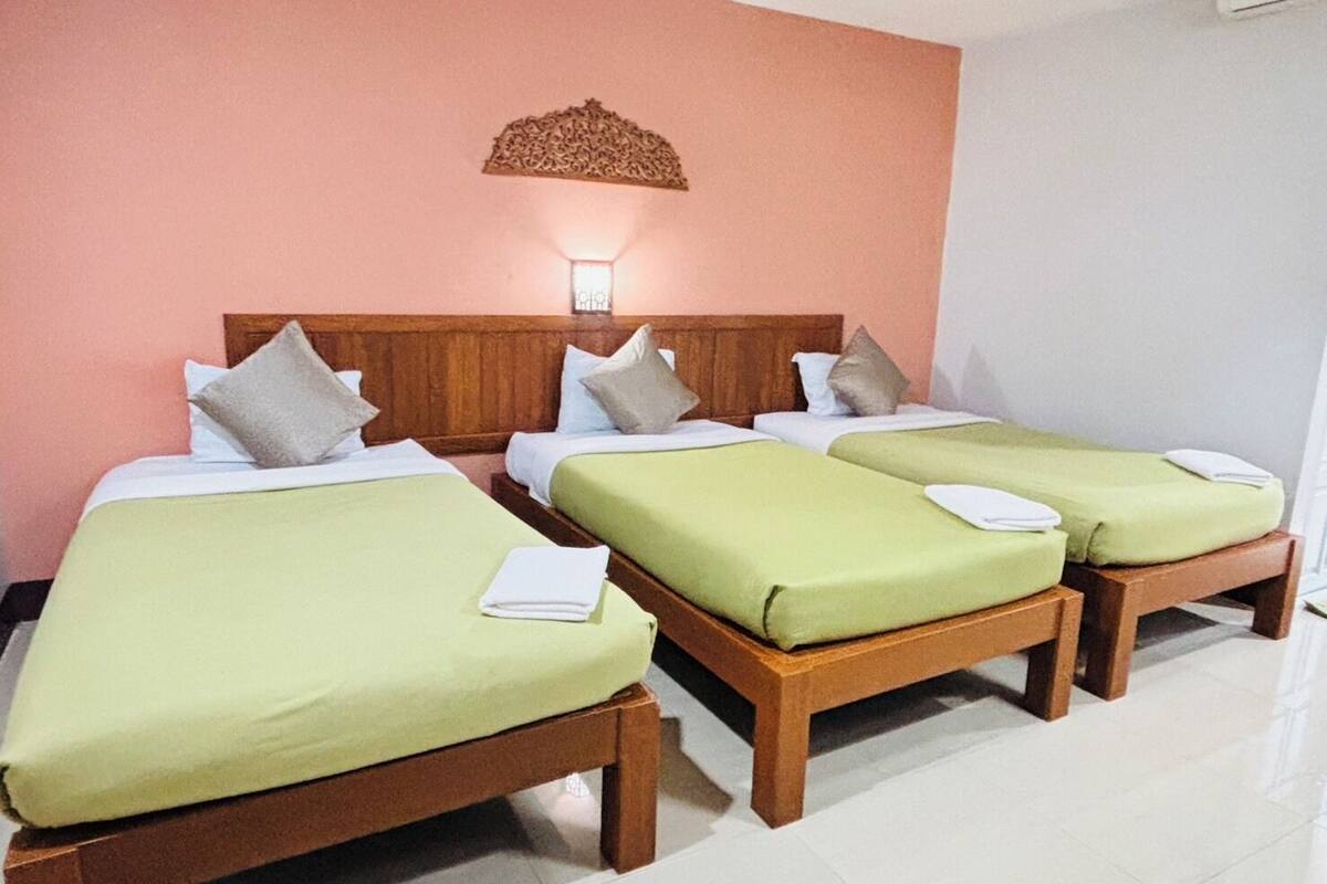 A hotel room with three single beds, wooden headboards, and a wall-mounted light fixture.