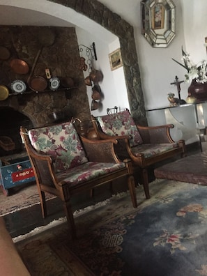 A room with two wooden chairs with floral upholstery, a stone fireplace, and a decorative mirror. - Furnished chalet with pool and fireplace in the center of Serra Negra. (Serra Negra)
